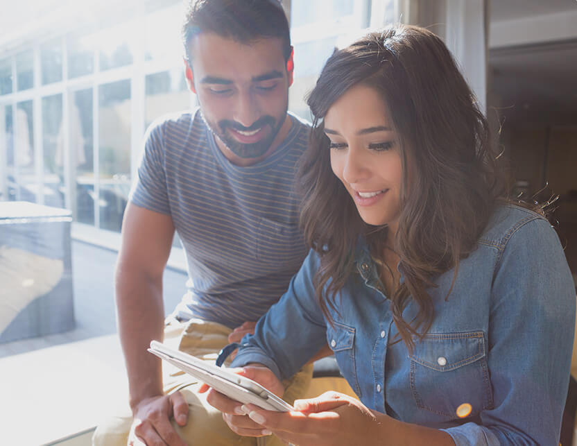 A couple of young people are looking at the tablet and smiling.